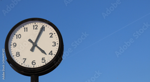 Retro style street clock on slightly blue sky background.