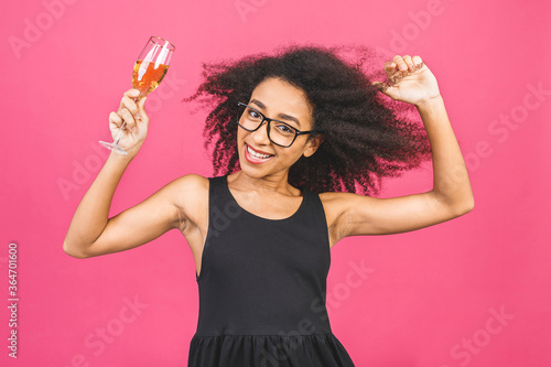 Happy birthday! Portrait of happy African-American black woman with glass of champagne isolated over pink background.
