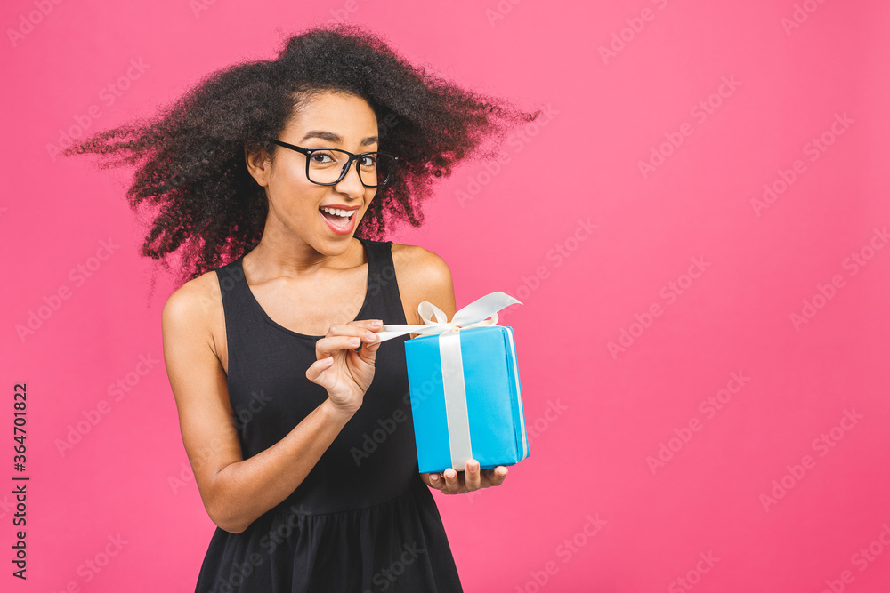 Happy african american curly lady in casual laughing while holding present isolated over pink background. Happy african american curly lady in casual laughing while holding present isolated over pink background.