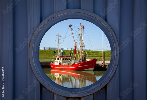 Durchblick  durch eine Öffnung in einer hölzernen Wand auf ein rotes Fischerboot im Hafen  photo