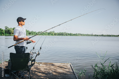 Young fisherman fishing on lake or river. Side view of adult guy fising at river or lake. Man holding rod in hands. Sunny beautiful day for getting fresh tasty fish.