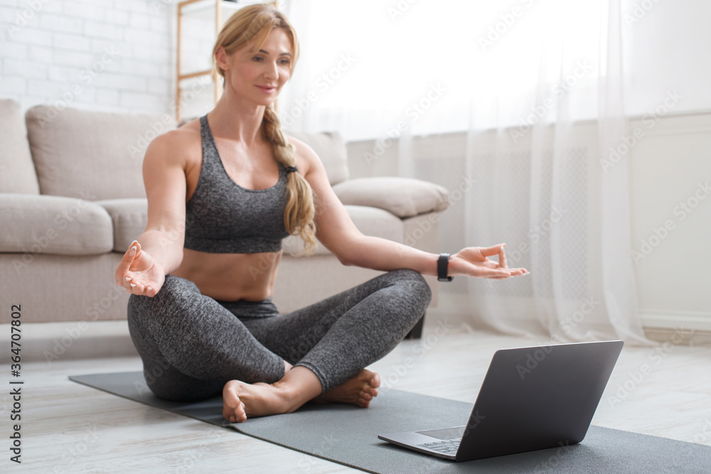 Fitness, yoga and pilates. Middle aged woman in sportswear doing yoga with laptop on mat Fitness, yoga and pilates. Middle aged woman in sportswear doing yoga with laptop on mat
