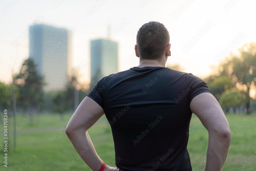  Attractive Man standing in a park after jogging. Back viev