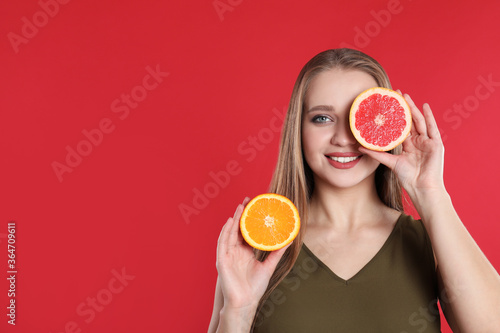 Young woman with cut orange and grapefruit on red background, space for text. Vitamin rich food