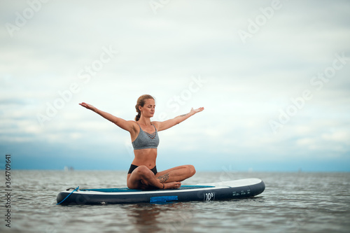 Woman practicing yoga on the paddle board in the morning