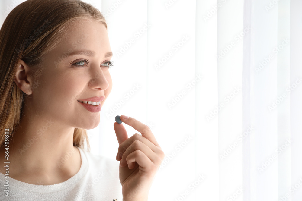Young woman taking vitamin pill indoors. Space for text Young woman taking vitamin pill indoors. Space for text