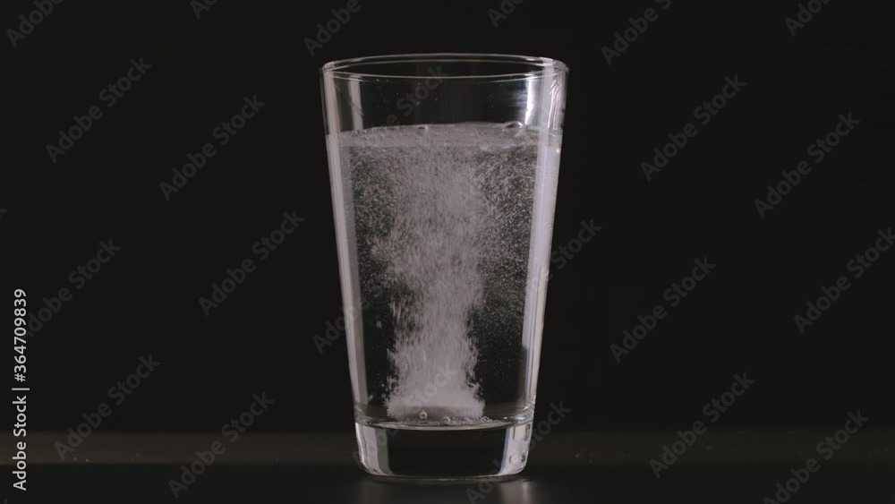 White instant pill falls into glass of water and dissolves White instant pill falls into glass of water and dissolves