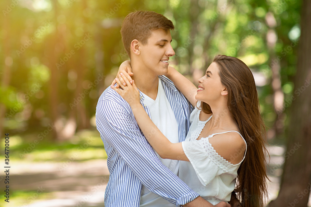 Handsome young man embracing his lovely wife at green park in summer, empty space Handsome young man embracing his lovely wife at green park in summer, empty space