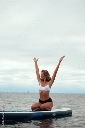 Woman practicing yoga on the paddle board in the morning