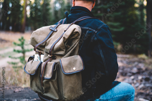 Cropped image of male traveler with backpack sitting in wood recreation on nature environment on free time adventure, caucasian hipster guy explorer discover trip in national park on vacations © BullRun