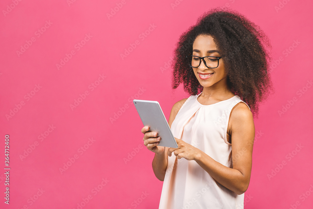 Young american student girl with curly african hair holding digital tablet and smiling standing over isolated pink background with copy space for text, logo or advertising. Young american student girl with curly african hair holding digital tablet and smiling standing over isolated pink background with copy space for text, logo or advertising.