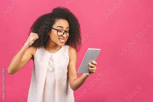 Happy african american girl looking excited looking at her tablet screen celebrating victory making winner gesture screaming and laughing. Success, happiness, joy concept.