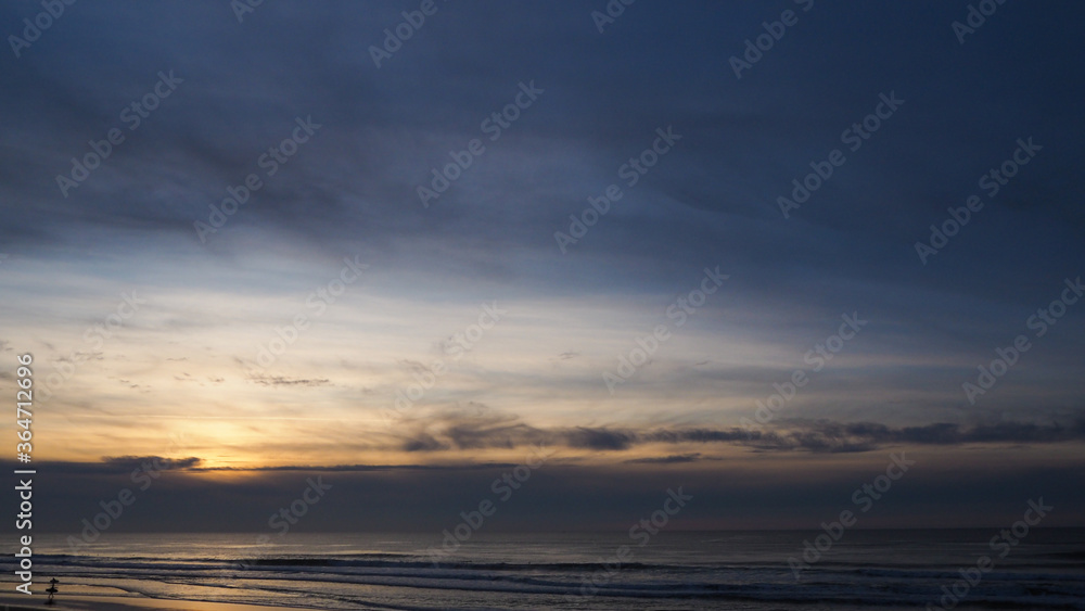 Coucher de soleil mélancolique sous un ciel voilé, avec quelques surfeurs sur la plage