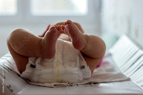 Baby girl lying on white sheet and holding her legs up in the air.Image of unrecognizable cute baby in dippers shaking feet while lying in bed innocence concept.A cropped shot of baby feet.Copy space.