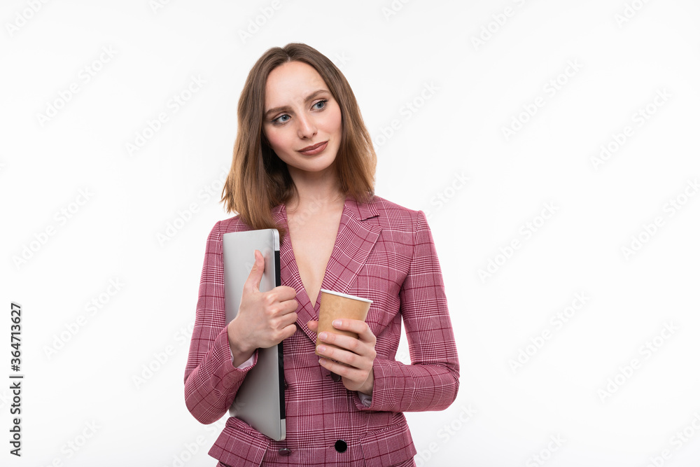 A beautiful girl in a pink jacket holds a laptop and drinks coffee on a white background. Business style