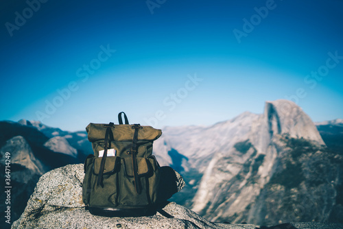 Trendy touristic backpack with convenient pockets for carrying staff and equipment on hiking tour in mountains, roll top khaki rucksack on high rock for active traveling lifestyle in nature landscape © BullRun