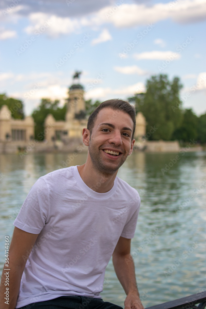 Photo of a young and attractive man with a white t/shirt standing next to the lagoon in Retiro park, Madrid