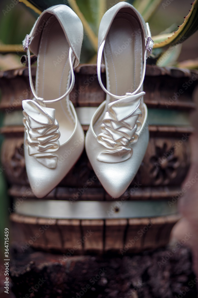 A pair of white elegant bride shoes standing on a plant vase A pair of white elegant bride shoes standing on a plant vase