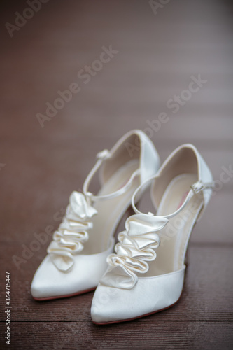 A pair of white elegant bride shoes on a brown woodenbackground