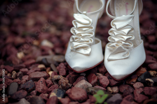 A pair of white elegant bride shoes sitting on brown rocks