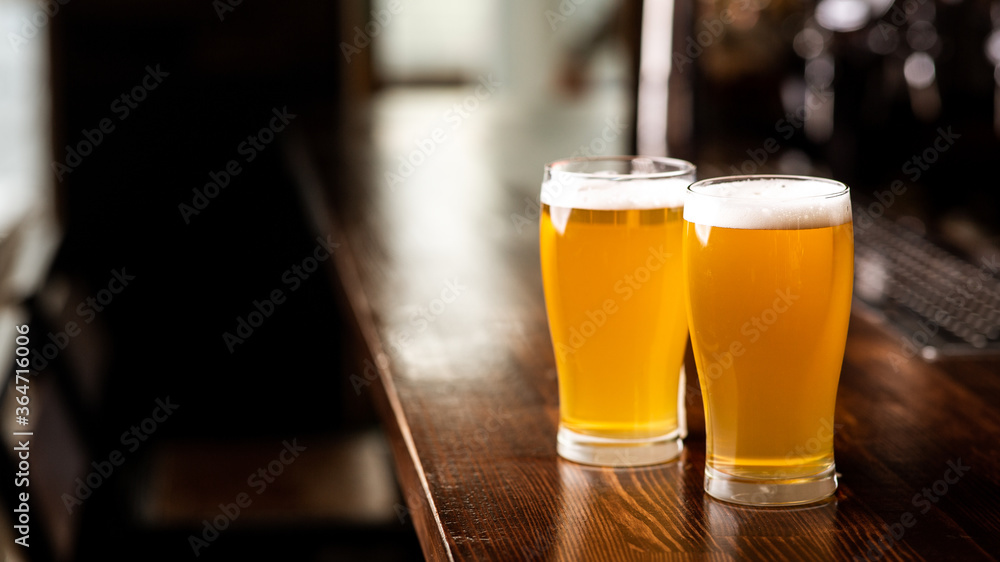 Hangouts with friends in pub and beer set. Two glasses of light beer with foam on wooden bar counter in daylight in interior of pub