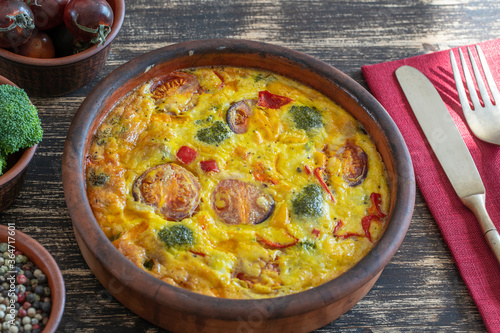 Ceramic bowl with vegetable frittata, simple vegetarian food. Frittata with egg, tomato, pepper, onion, broccoli and cheese on wooden table. Italian egg omelette