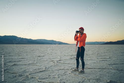 Skilled woman traveler making photo on camera exploring wild lands in death valley, professional female photographer taking image of evening sunset and landscape having trip in Badwater basin.