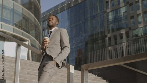 Wallpaper Mural Medium shot of good-looking African businessman wearing elegant clothes standing outdoors on stairs leaning on railing, drinking coffee and looking around Torontodigital.ca