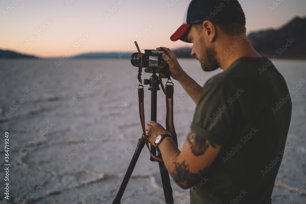 Skilled male photographer making settings on digital camera taking picture of landscape of Badwater basin,professional cameraman shooting scenic dawn in wild environment of dry lake in Death valley.