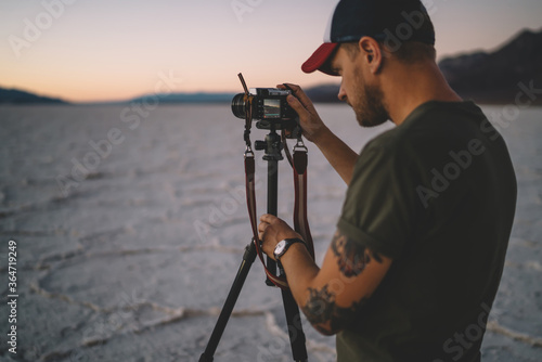 Fototapeta Naklejka Na Ścianę i Meble -  Skilled male photographer making settings on digital camera taking picture of landscape of Badwater basin,professional cameraman shooting scenic dawn in wild environment of dry lake in Death valley.
