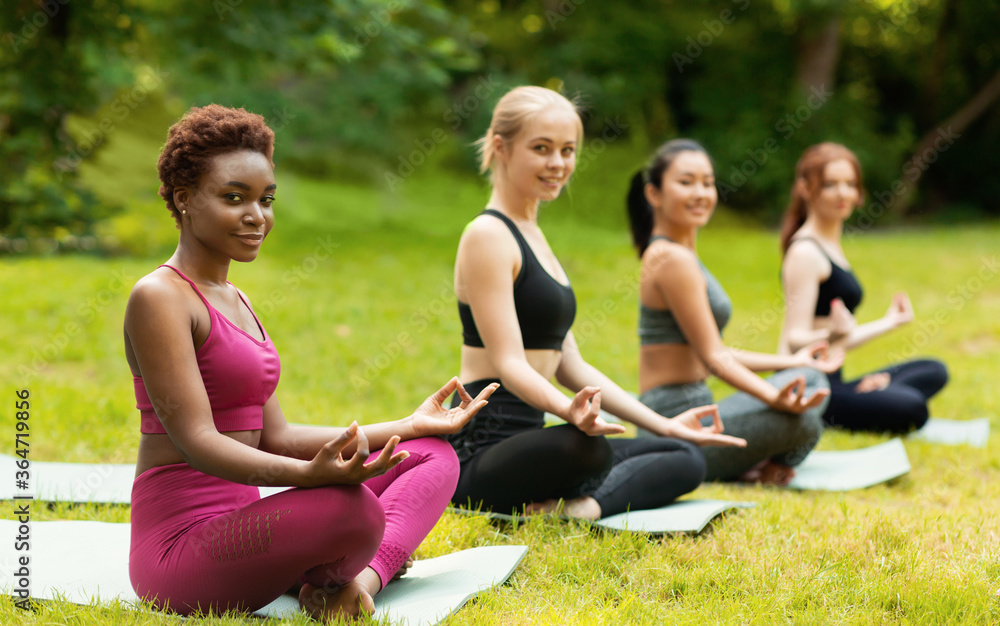 Multiracial girls having their morning yoga class outdoors, meditating in lotus pose. Copy space