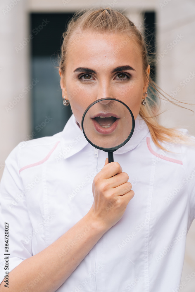 The dentist is a young beautiful girl holding a magnifying glass in her hands opening her mouth The dentist is a young beautiful girl holding a magnifying glass in her hands opening her mouth