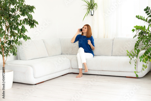 girl talking on the phone. Smiling real woman at home. White interior, copy space