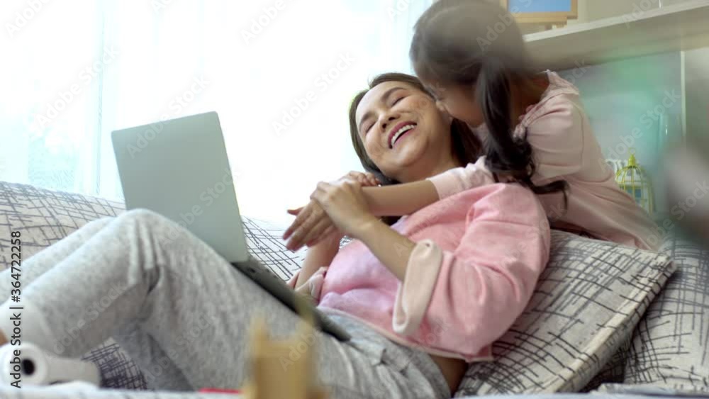 A Beautiful Asian mother busy working from home while looking after and teaching her children home work on a laptop computer A Beautiful Asian mother busy working from home while looking after and teaching her children home work on a laptop computer
