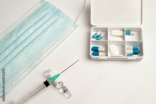 coronavirus (covid-19) vaccine concept syringe with glass container, protection mask and medicine pillbox, white background, top view