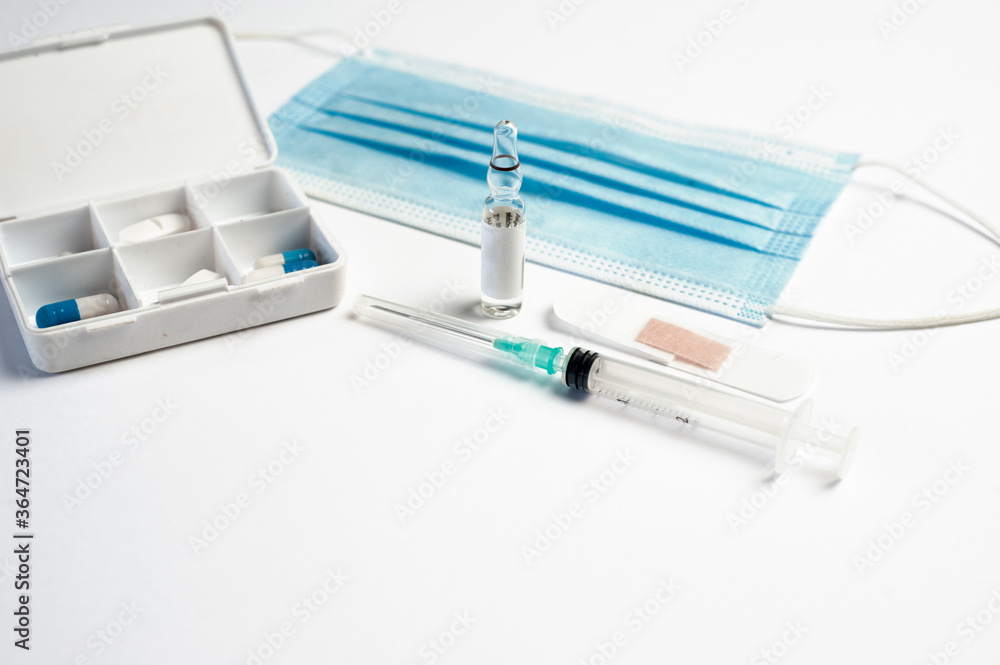 coronavirus (covid-19) vaccine concept syringe with glass container, protection mask and medicine pillbox, white background, top view