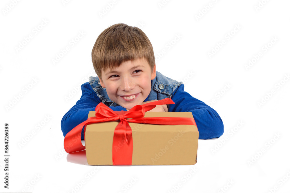 the boy is sitting at the table, in front of him is a gift in paper packaging with a red ribbon the boy is sitting at the table, in front of him is a gift in paper packaging with a red ribbon