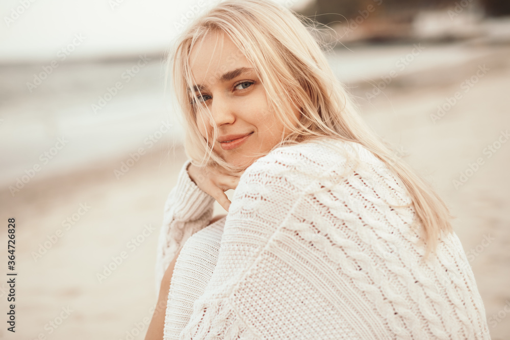 Smiling blonde woman in warm sweater sitting on beach Smiling blonde woman in warm sweater sitting on beach