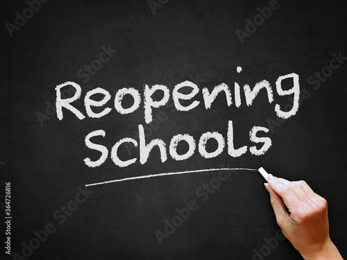 A hand writing 'Reopening Schools' on chalk board for schools reopening plans after Covid-19 (Coronavirus) pandemic lockdown. photo