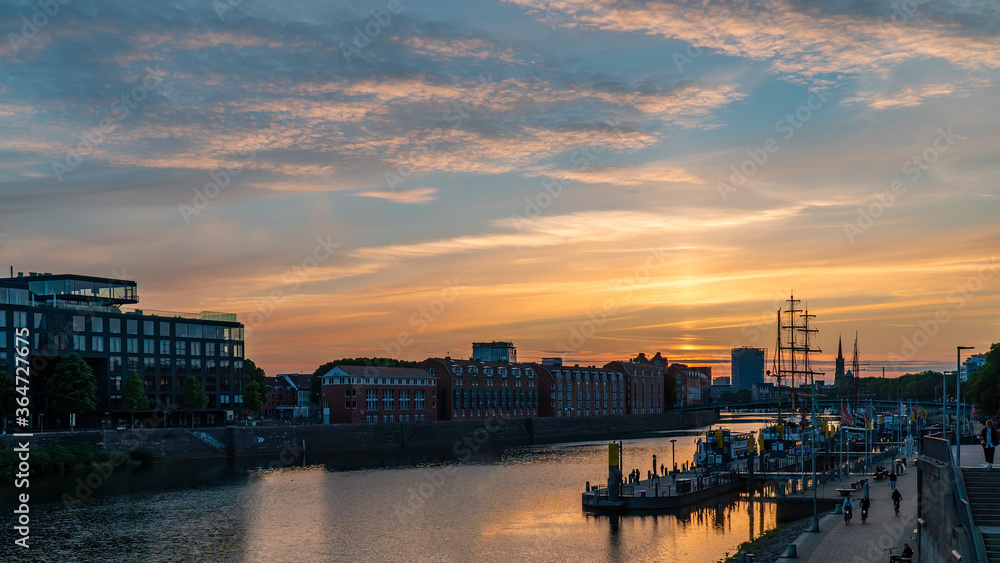Fototapeta premium Sunset in summer landscape view blue orange sky in Europe Bremen Germany tourism landmark sightseeing in Schlachte weser river with old vintage boat ship medieval