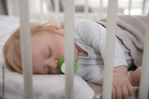 Cute little baby with pacifier sleeping in crib. Bedtime