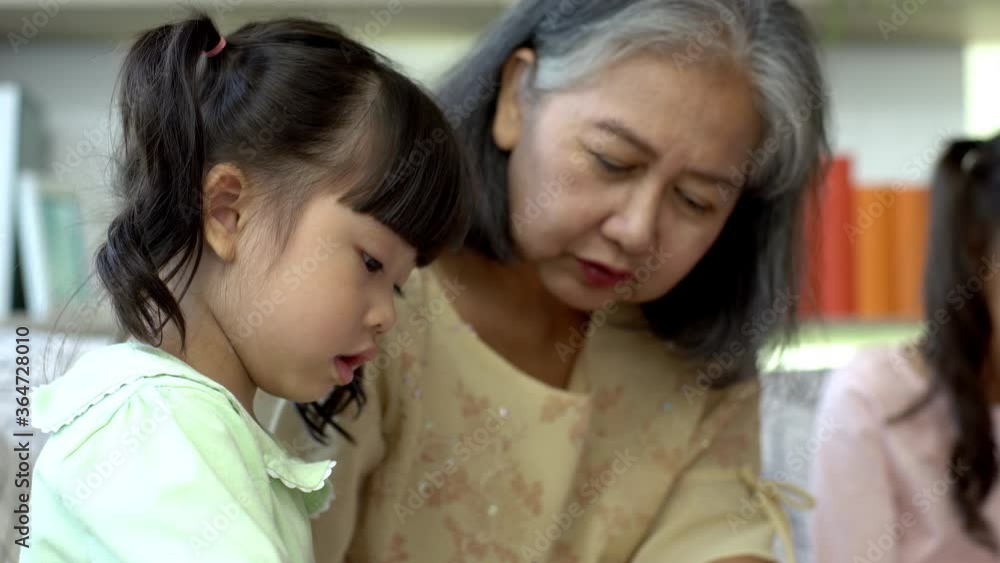 A kind and gentle Asia grandmother teaching her granddaughter to read write and drawing on a white board at home A kind and gentle Asia grandmother teaching her granddaughter to read write and drawing on a white board at home