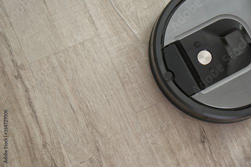 Modern robotic vacuum cleaner on wooden floor, top view. Space for text
