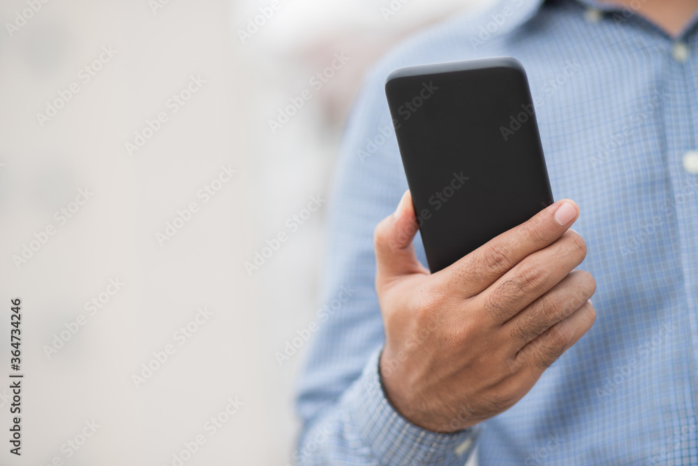 Close up male hands holding using black smartphone on city background. Close up male hands holding using black smartphone on city background.