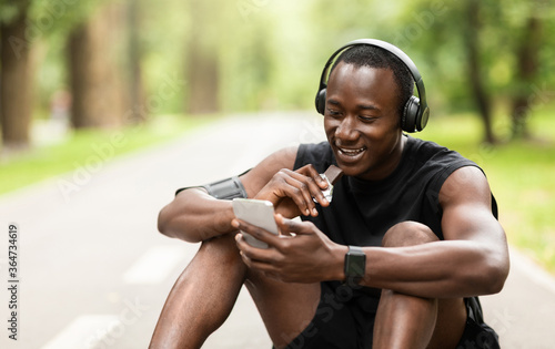 Positive black sportsman eating protein bar while resting photo