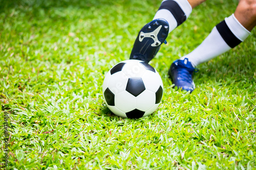 Selective focus to ball with blurry soccer player run to shoot it on green grass. Shoot soccer ball.