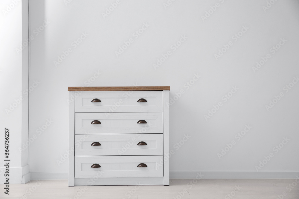 Fototapeta premium Modern white chest of drawers near light wall in room, space for text. Interior design