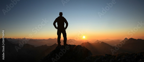 Man Silhouette reaching summit enjoying freedom and looking towards mountains sunset. Allgau Alps, Bavaria, Germany and Tyrol Austria.
