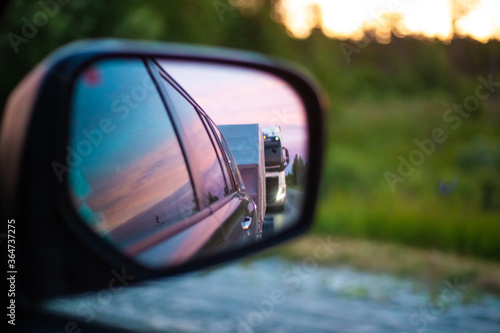 reflection in a side mirror of a distant mode of transport going along the highway at sunset