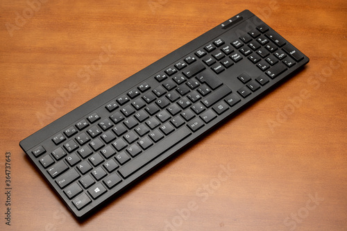 Teclado sem fio, de computador, pc, na cor preta, com letras e números brancos, em cima de uma mesa de madeira. Home Office. 